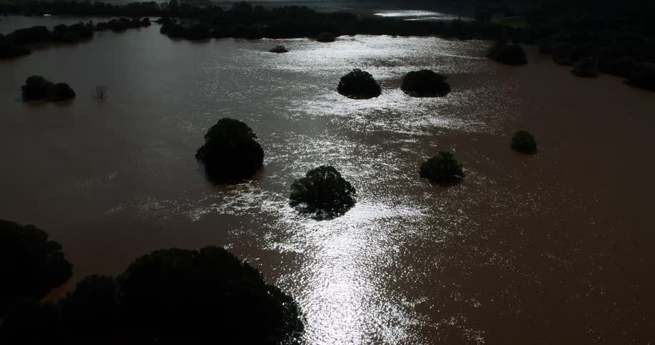 Flood waters surrounding groves of trees reflect the moonlight in the evening