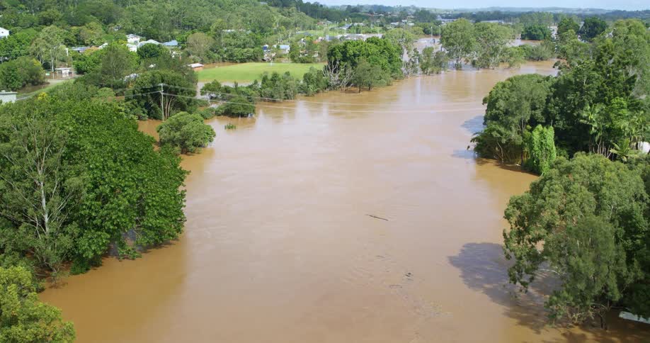 Aerial view of a residential area submerged in muddy floodwaters with trees and houses partially underwater