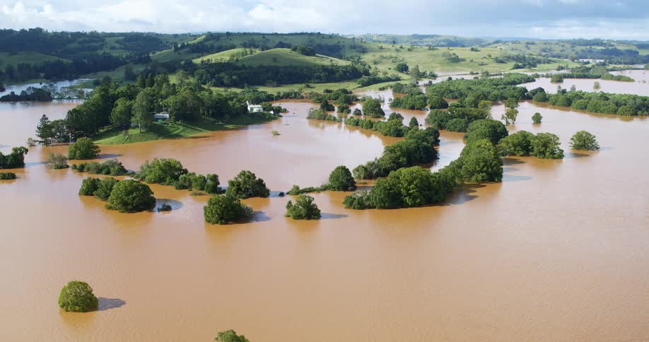 Treetops stand above the flood water with buildings on high ground on the hills