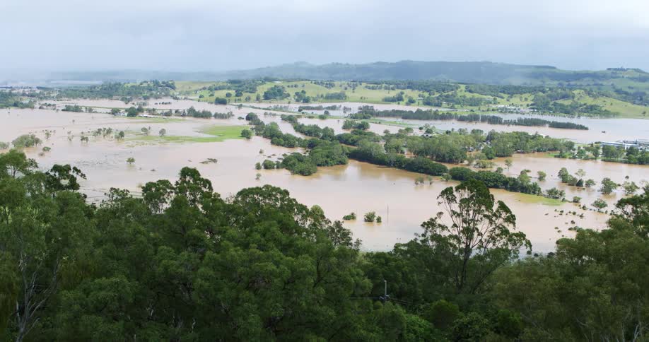 An elevated view captures a widespread flood event where vast expanses of lowlying brown water surround small patches of high ground and trees the scene is dominated by a mix of flooded fields small groupings of buildings and a backdrop of green ro