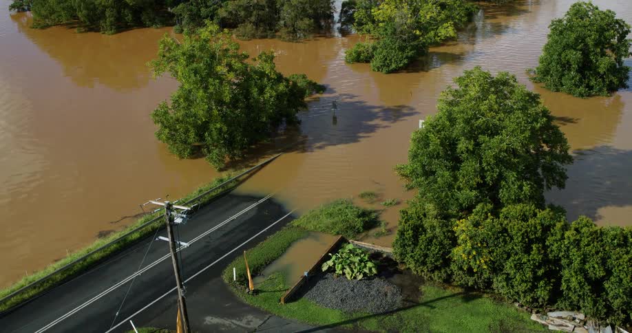 From an aerial perspective a rural road disappears into deep murky floodwaters that have completely engulfed the surrounding landscape leaving only treetops visible