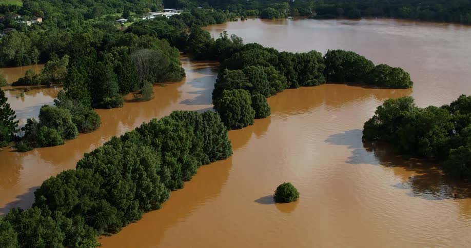 Aerial view of muddy floodwater covering land around clusters of green trees