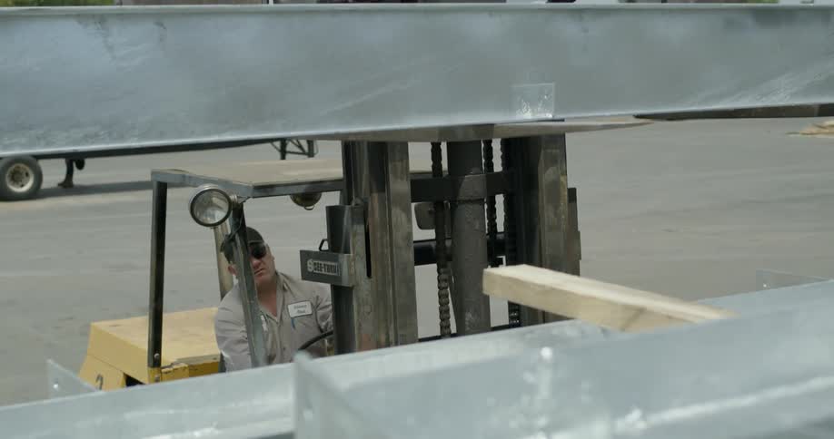 A man uses a vehicle to move some steel beams