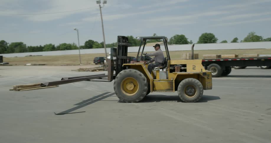 A man moves metal beams with a forklift