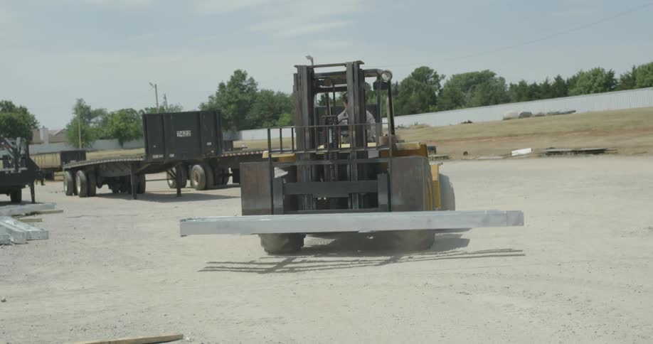 A man operates a forklift and moves a metal beam