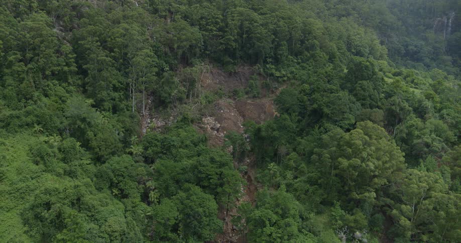 An aerial shot reveals a massive landslide that has carved a path of destruction down a lush green mountainside leaving a raw scar of exposed earth and rock