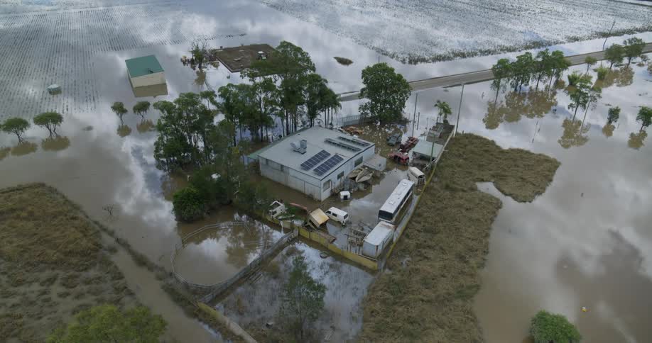 Rural complex surrounded by floodwater shows buildings trees and access roads partially submerged