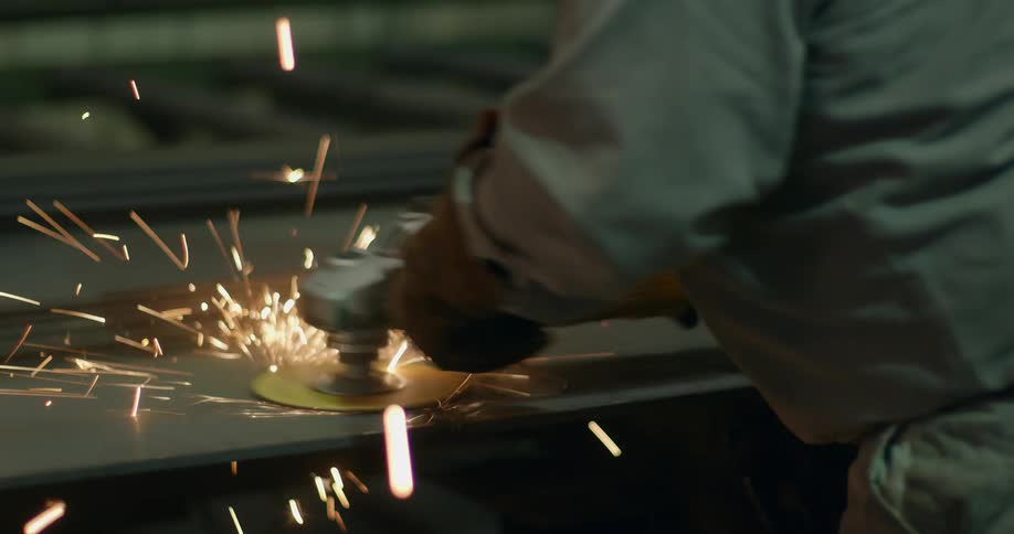 A welder using a tool to work on a piece of metal with sparks flying