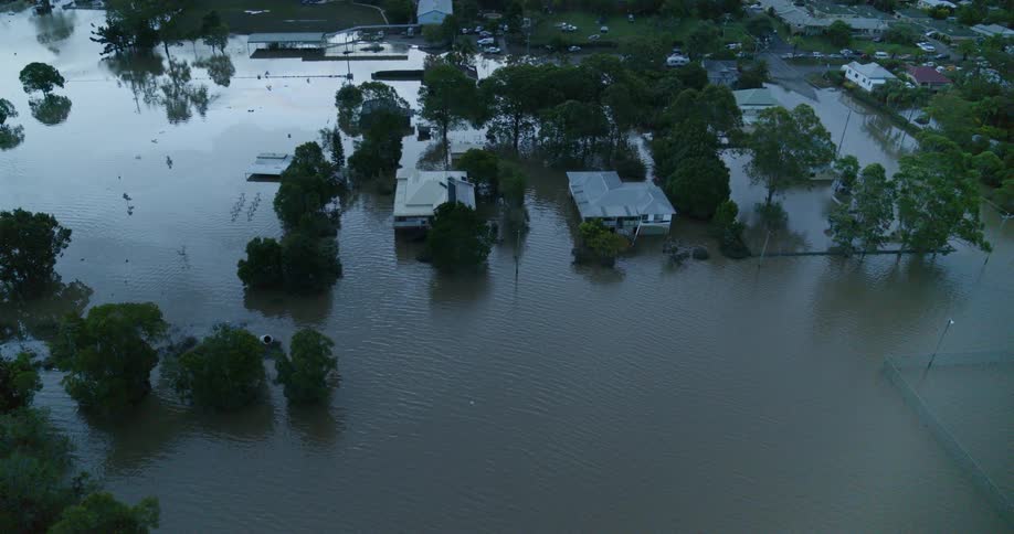 An aerial view shows a wide area of suburban homes and trees partially submerged by extensive murky floodwaters during an ongoing natural disaster