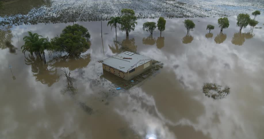 Isolated rural house appears surrounded by floodwater with partially submerged trees around it