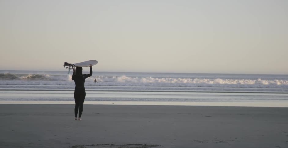 A woman holds a surfboard on her head while looking at the ocean
