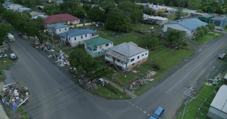 An aerial view shows a residential intersection lined with piles of debris as trucks pass through the neighborhood