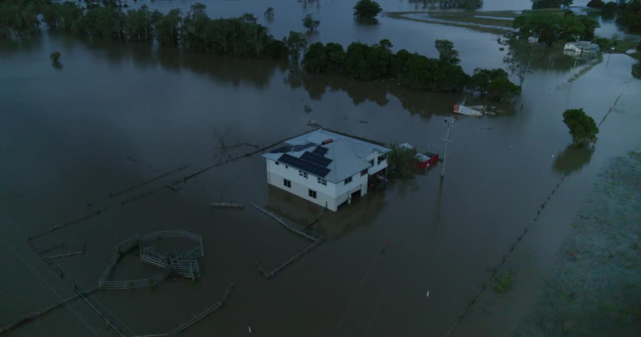 Twostory rural building partially submerged in flooded area with fences and surrounding trees