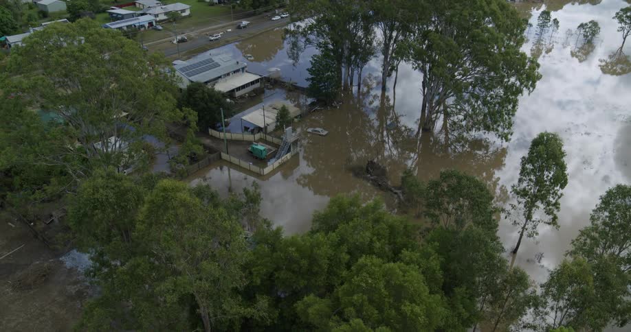 Trees stand above the flooded neighborhood with submerged cars and yards as a van moves on a street