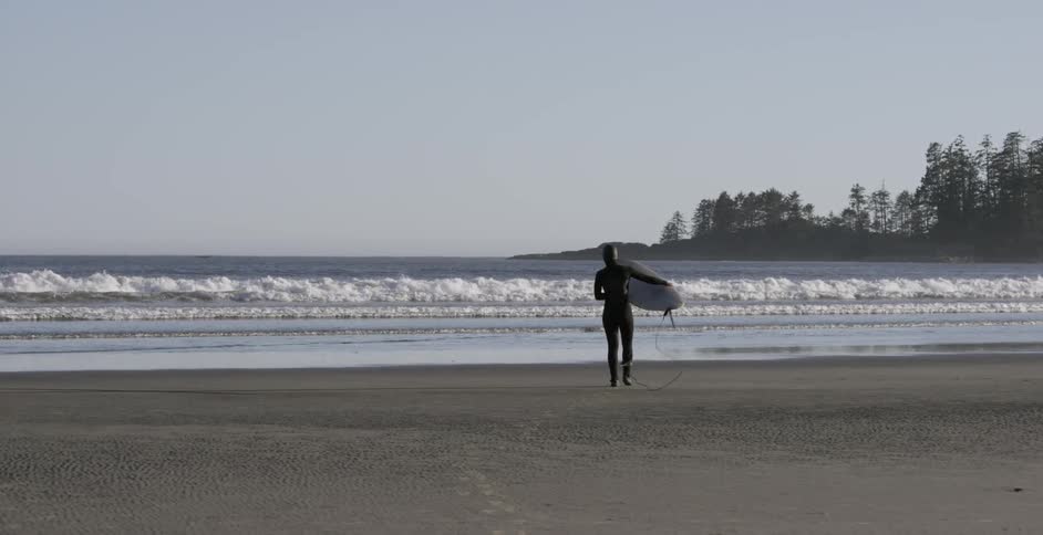 Person in wet suit carrying surfboard on beach toward the ocean