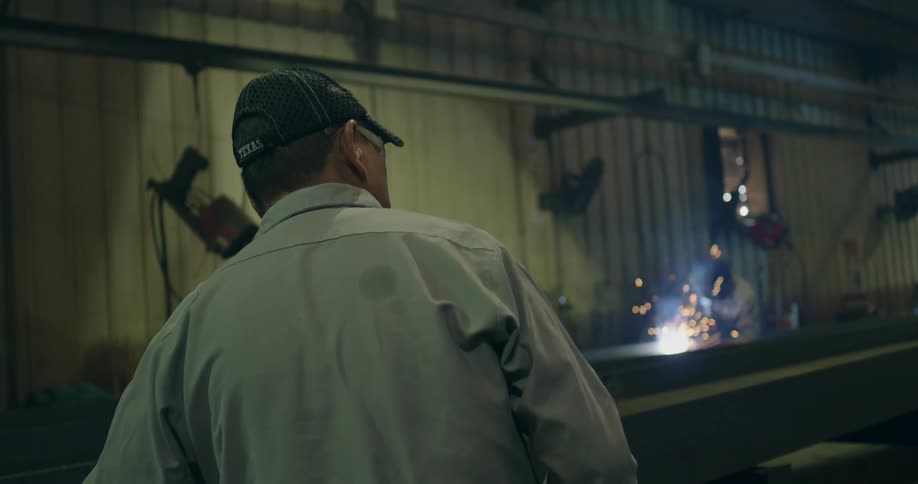 A man walks through a workshop where men are working and sparks are flying