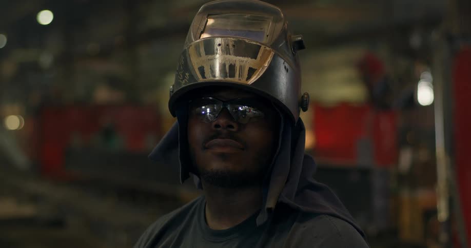A man opens his welding mask in a shop