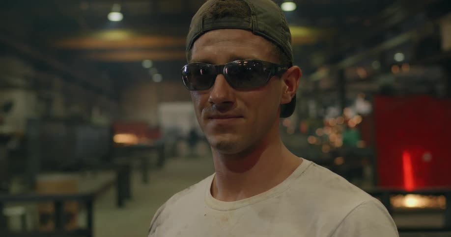 A man stands in a factory with sparks flying in the background