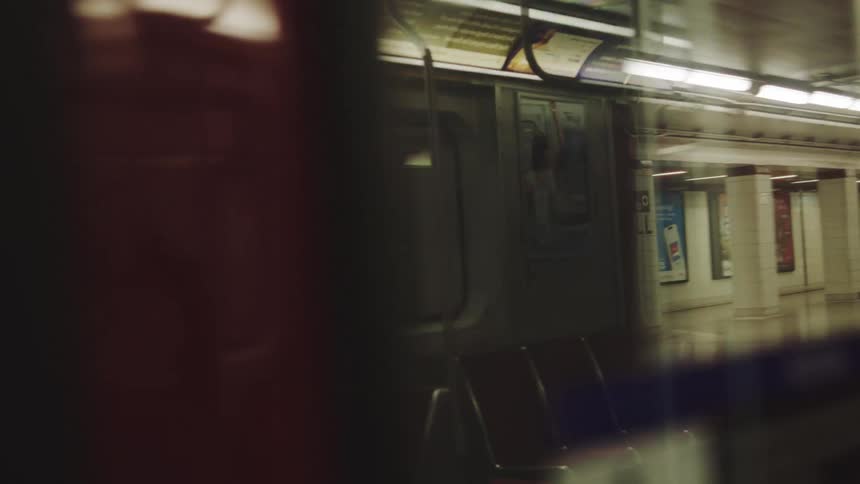 The interior of a subway car reflects the passing view of an underground station platform as the train begins to move