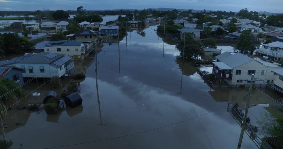 An aerial shot reveals a residential street completely submerged by dark floodwater with water levels reaching the first floor of houses