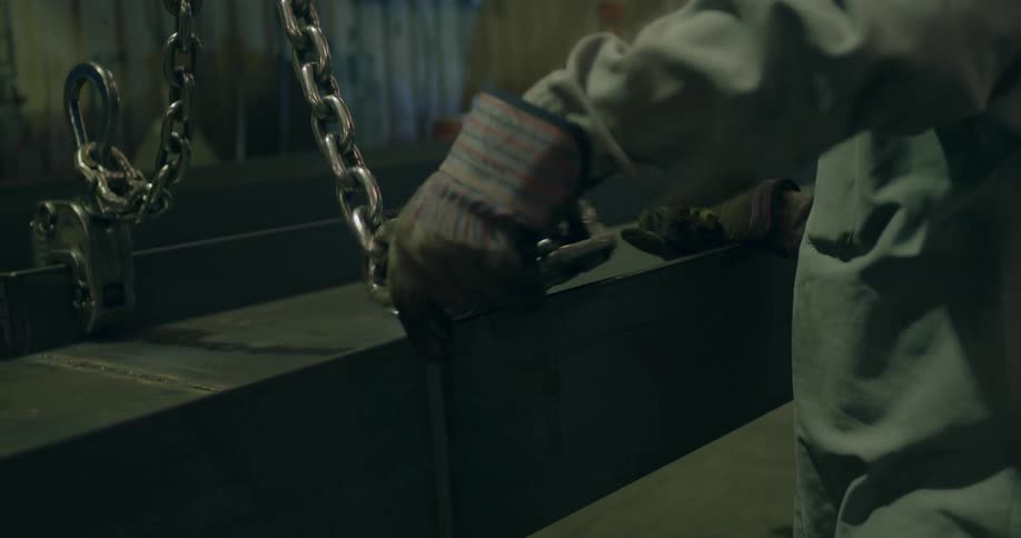 A man unhooks a metal beam in a factory