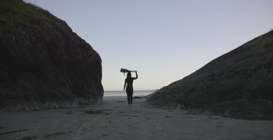 A woman carries a surfboard towards the water