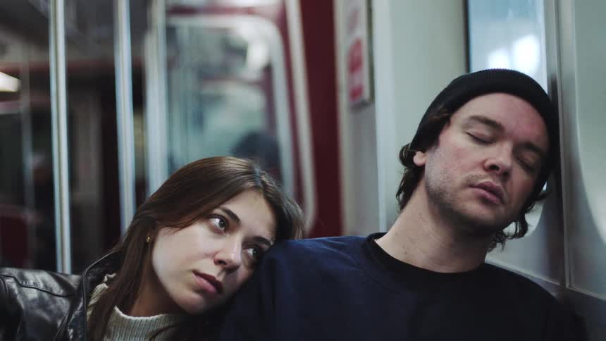 Woman resting her head on the shoulder of a sleeping man inside a subway car