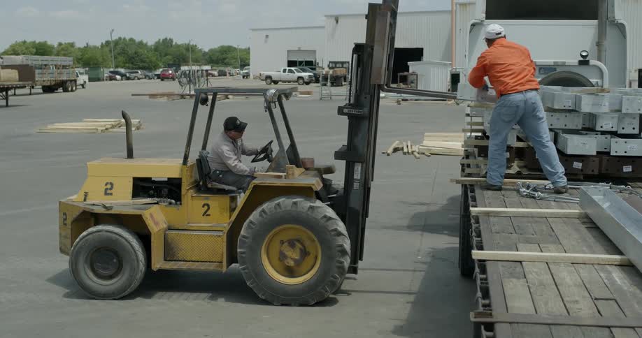 A man drives a forklift and loads materials onto a truck