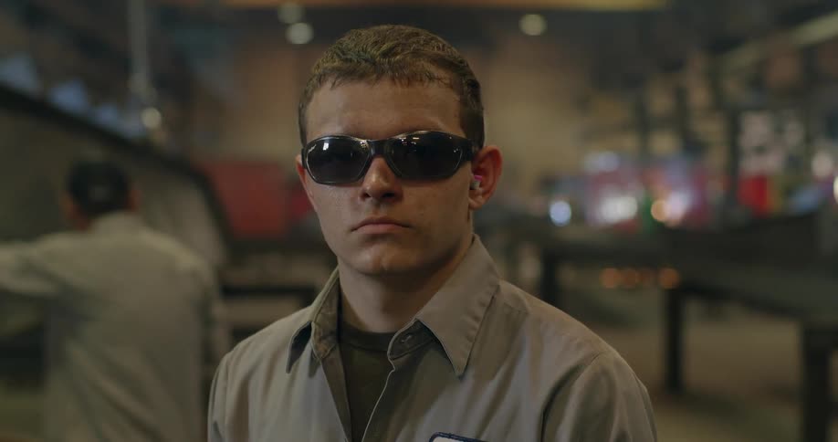 A man with dark sunglasses stands in a shop as others work