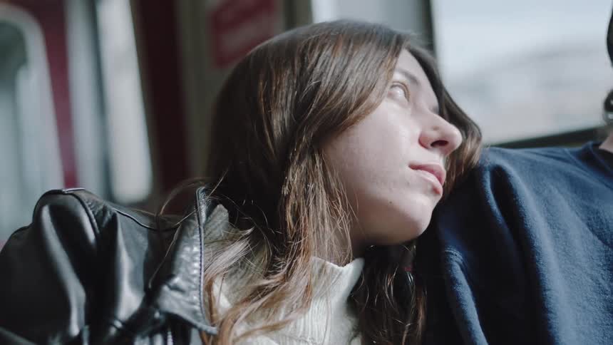 Woman resting her head on another persons shoulder while looking out a train window