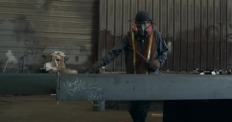A man spray paints a metal beam in a factory
