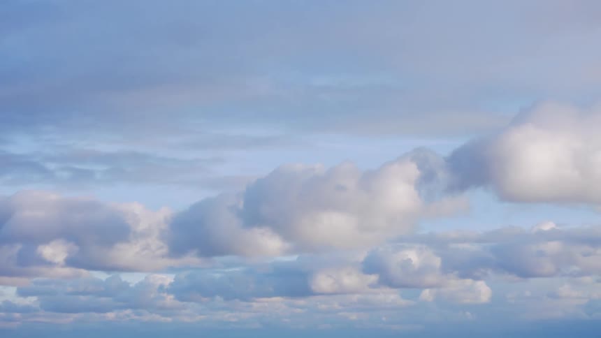 Soft fluffy clouds drift lazily across a serene blue sky above the calm ocean