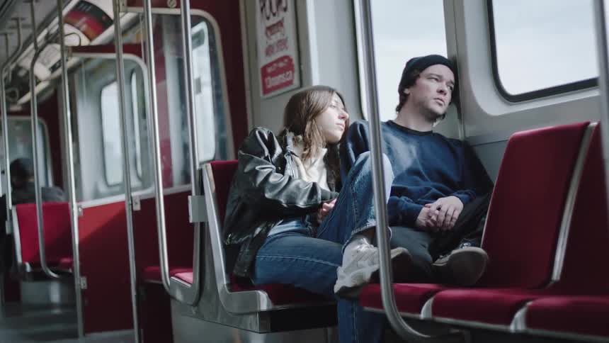A young couple sits together leaning and gazing contemplatively out the train window
