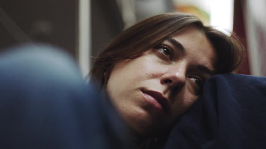 Focus shifts from a hand gently resting on dark blue fabric to reveal the weary contemplative expression of a young woman leaning her head against a shoulder