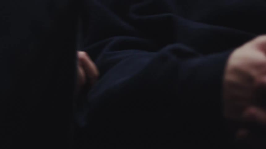 A persons hands are intertwined and the person is wearing black clothing