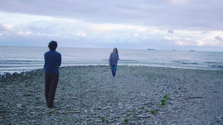 Young adult woman walking next to the coast and taking pictures of the ocean and later of a young adult male next to her outdoors