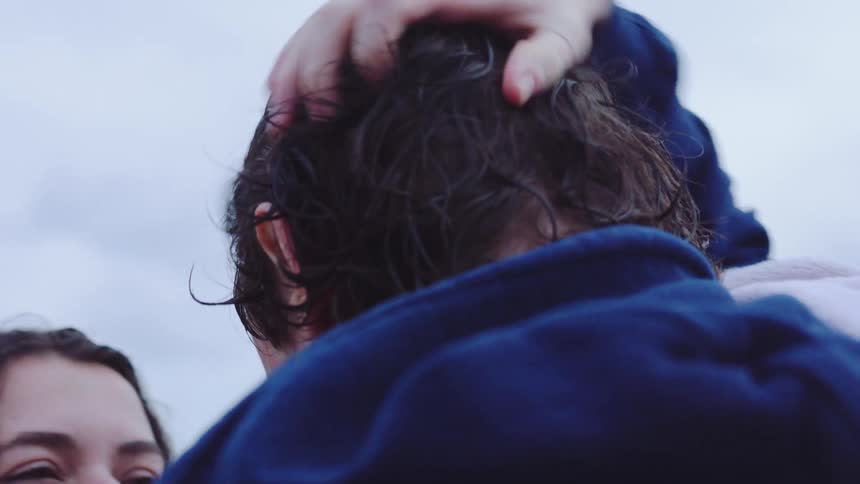 Couple looks at each other closely by the seaside as one person touches the others face