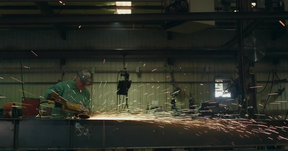 A man uses a tool in a factory while sparks fly all around