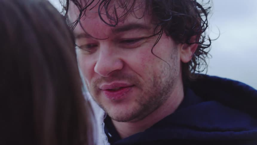 The face of a man with partially wet hair is looking ahead where someone is running their hand over his ear