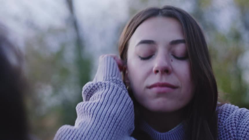 A woman in a sweater sits outside while talking with another woman