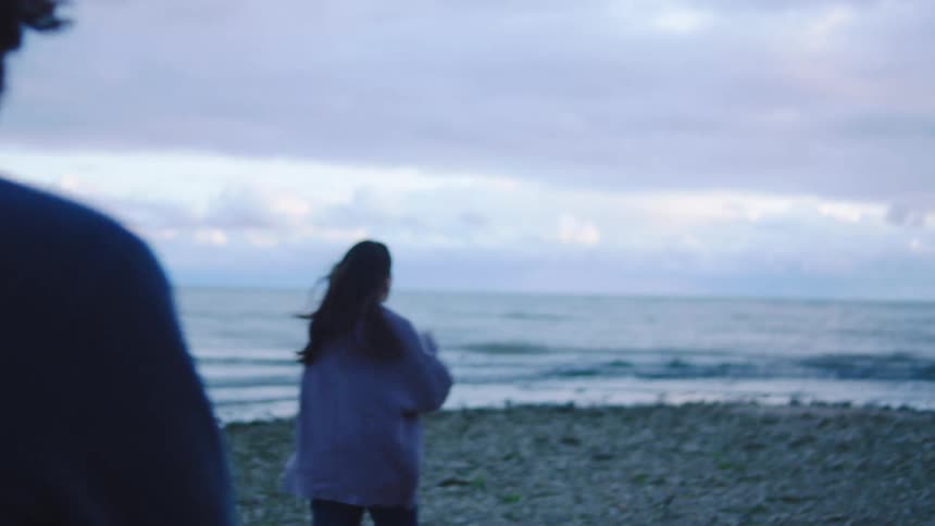 Woman takes a picture while walking on the shore with a man on a windy day