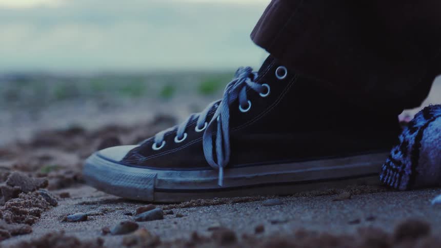 A worn black sneaker with faded laces sits on the sand hinting at a quiet outdoor moment