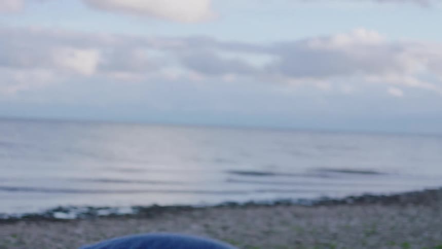 Person throws a stone toward the sea under a partly cloudy sky