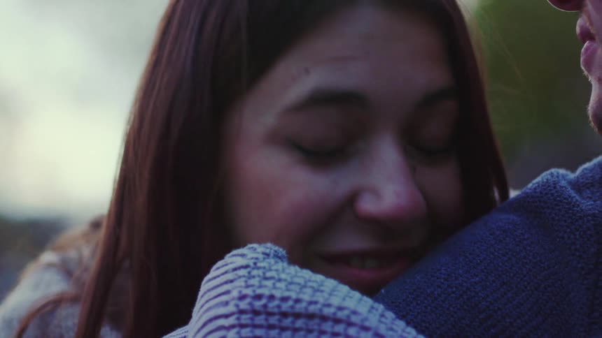 Young adult woman talking to a man while smiling and leaning her head against his arm outdoors during dusk or dawn