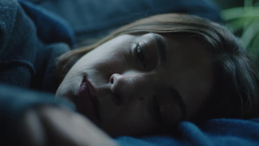 Closeup of a sad woman lying down softly illuminated by dim light