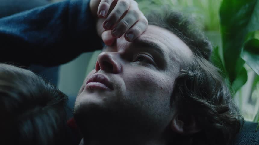 Face turned upward with hand on forehead and head resting on shoulder in leafy setting