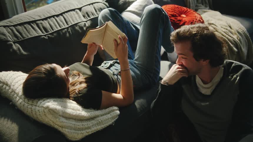 Couple reading books while seated on a sofa lit by daylight