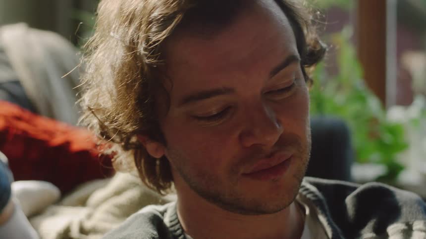 A man glances at the woman lying beside him before looking down at the open book in his hands