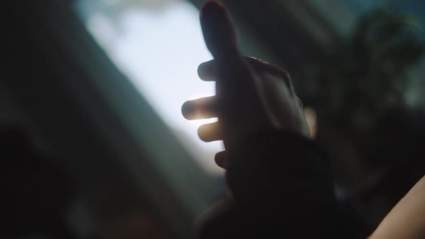 Hand extended toward bright light with blurred background of window and foliage