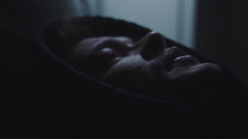 The face of a man wearing a hooded coat looking upwards in a dark environment